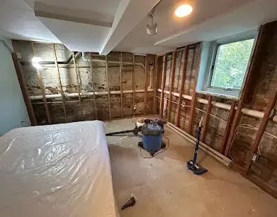 Walls stripped to the studs with plastic sheeting hung and a wet vacuum standing by