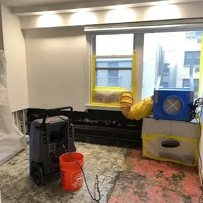 A dehumidifier and an air mover drying out a room after the damaged flooring was pulled up, leaving the bare floor exposed
