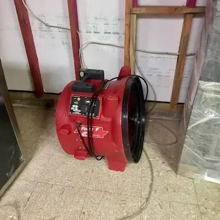 A red air mover running in a room with the lower wall opened and plastic sheeting hung to contain the drying area