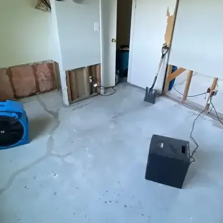 Air movers and a dehumidifier running in a room with the lower drywall removed and the floor left bare to dry