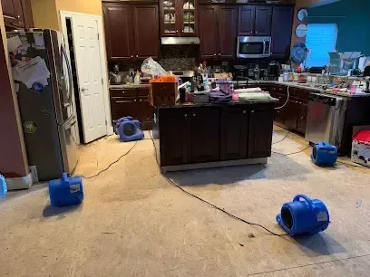 Air movers aimed across a kitchen floor drying out an appliance leak