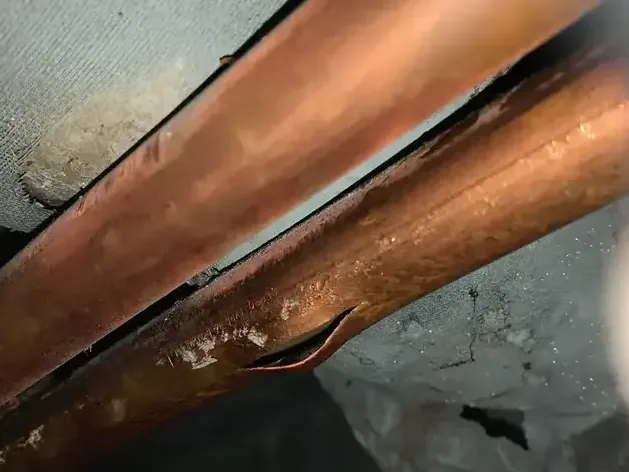 A copper supply pipe split open above a ceiling after it burst