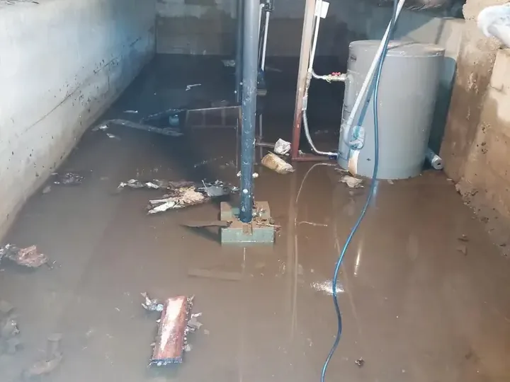 A tank water heater sitting in standing water on a flooded utility floor